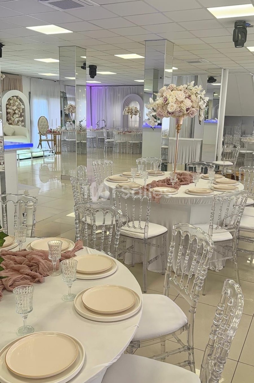 Salle de réception élégante avec tables dressées, chaises transparentes et décoration florale raffinée.