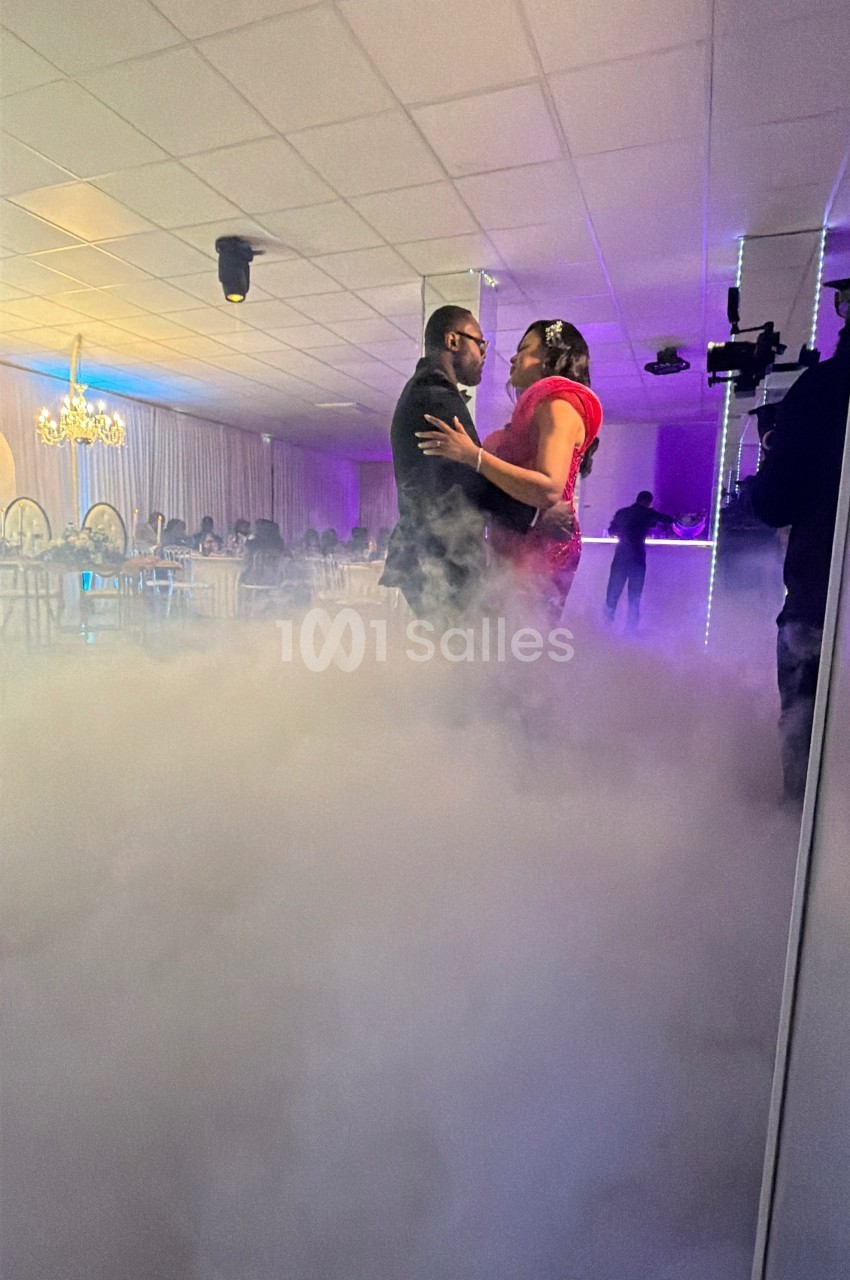 Un couple danse au milieu d'une piste entourée de fumée, dans une salle éclairée par des lumières tamisées.