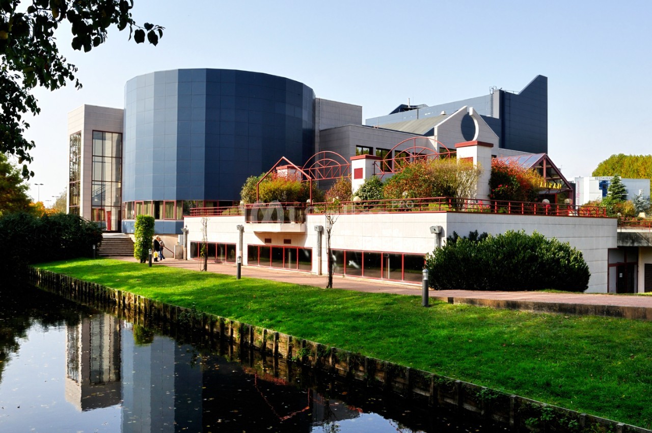 Bâtiment moderne aux façades blanches et bleues avec toiture en dôme - espace gazonné et canal en premier plan.
