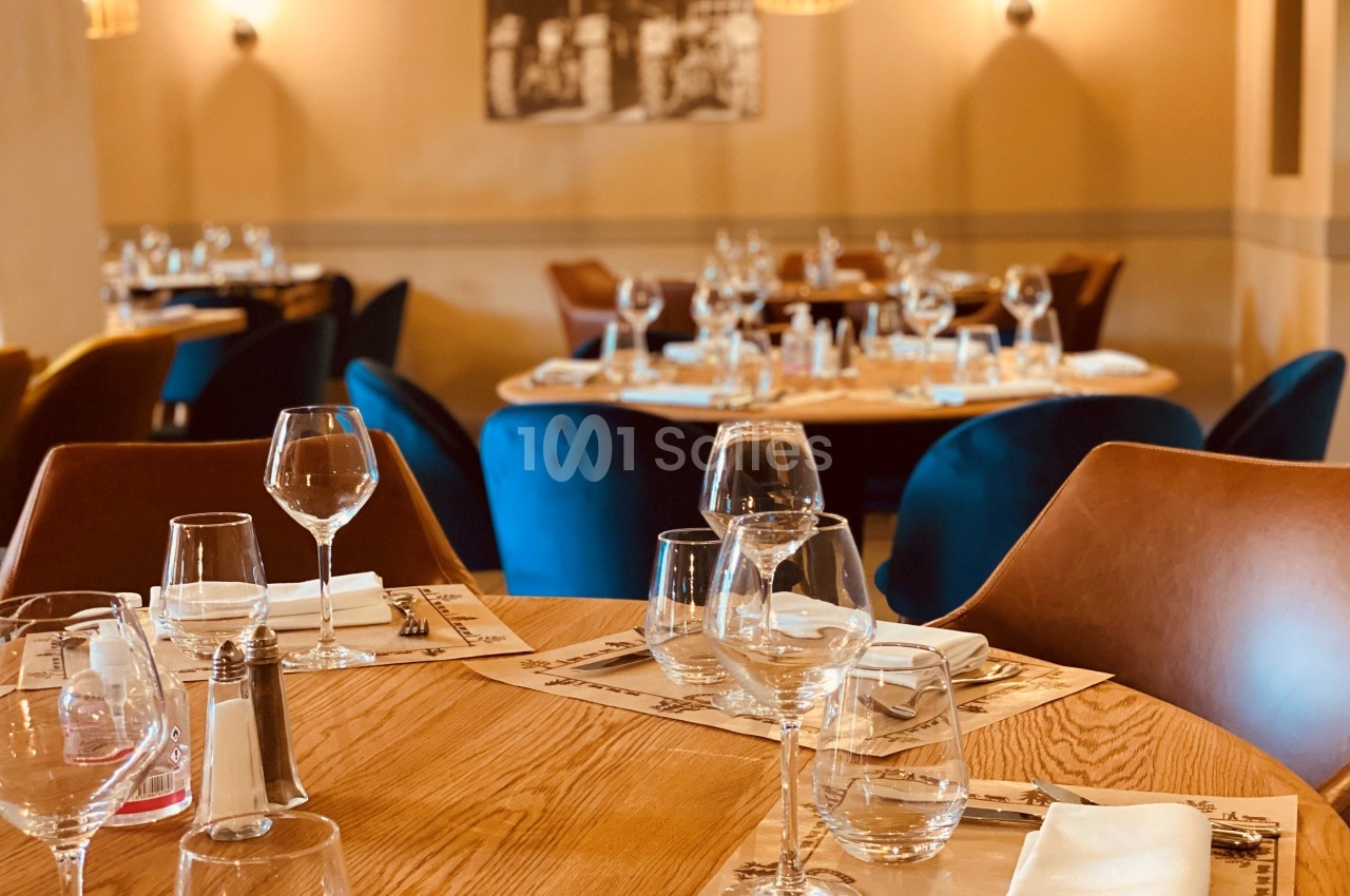 Salle de restaurant élégante avec tables en bois dressées, verres et serviettes, éclairage chaleureux.