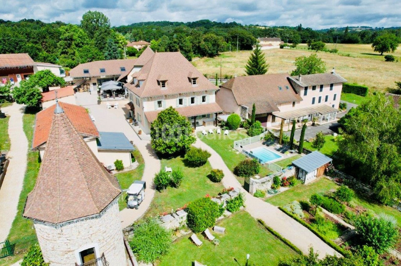 Vue aérienne d'un domaine avec bâtiments en pierre, piscine, jardins verdoyants et paysage rural environnant.