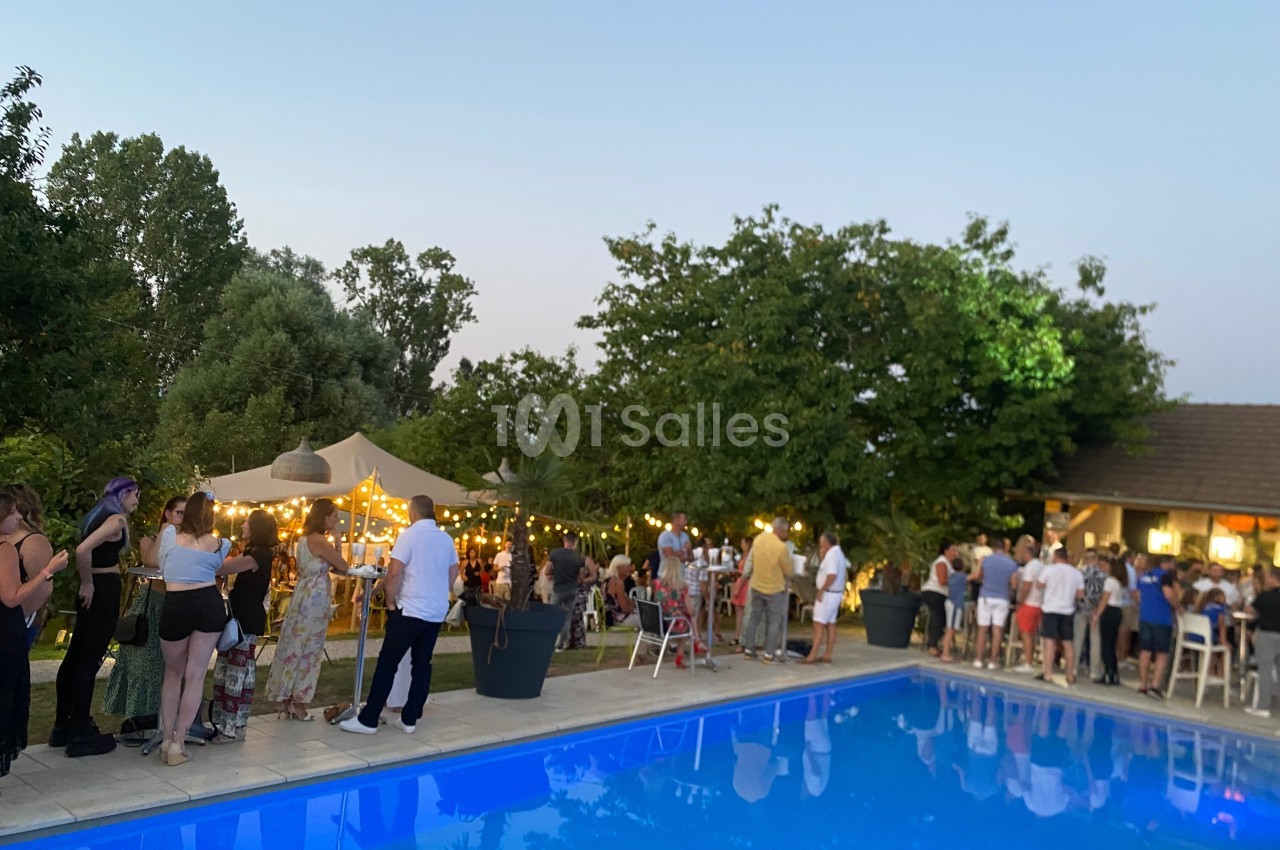 Groupe de personnes rassemblées près d'une piscine au crépuscule, avec guirlandes lumineuses et tentes dans un jardin.