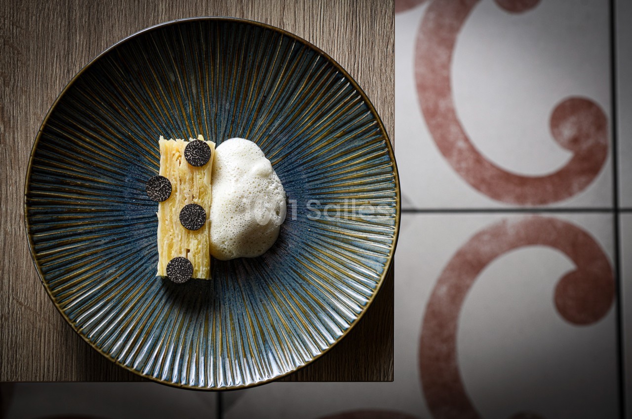 Assiette contenant un millefeuille de pommes de terre garni de truffes noires et accompagné d'une mousse légère.