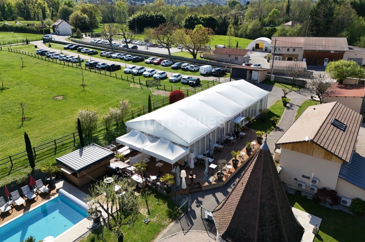 Vue aérienne d'une terrasse couverte entourée de verdure, avec une piscine et un parking à proximité.