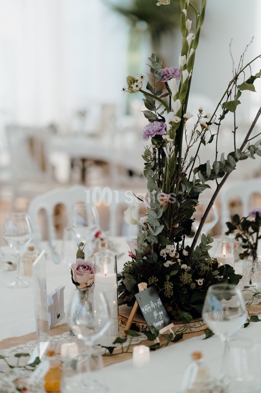 Centre de table floral avec des bougies, des verres et une petite ardoise sur une table dressée élégamment.