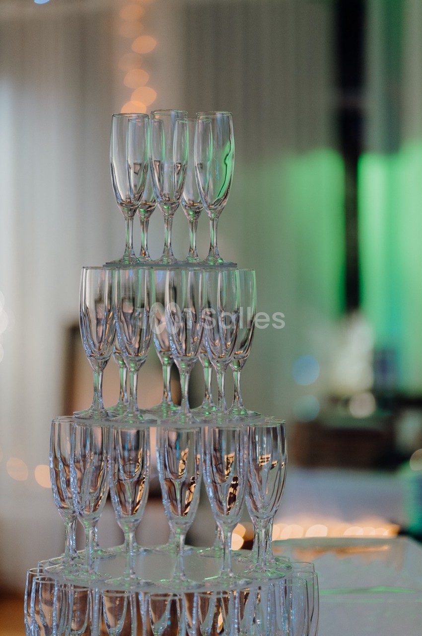 Pile de flûtes à champagne en verre disposées en pyramide dans un environnement lumineux et festif.