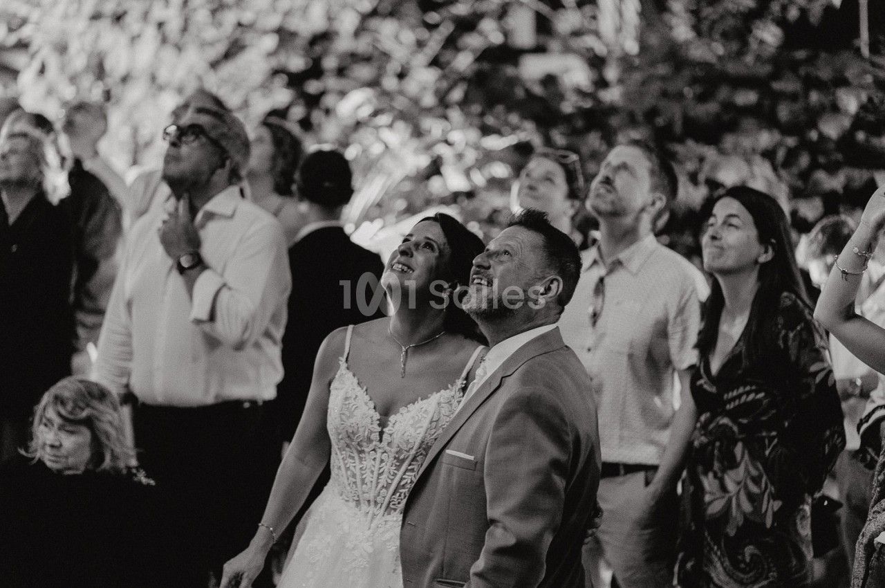 Un couple en tenue de mariage regarde vers le ciel, entouré d'invités lors d'une célébration en extérieur.