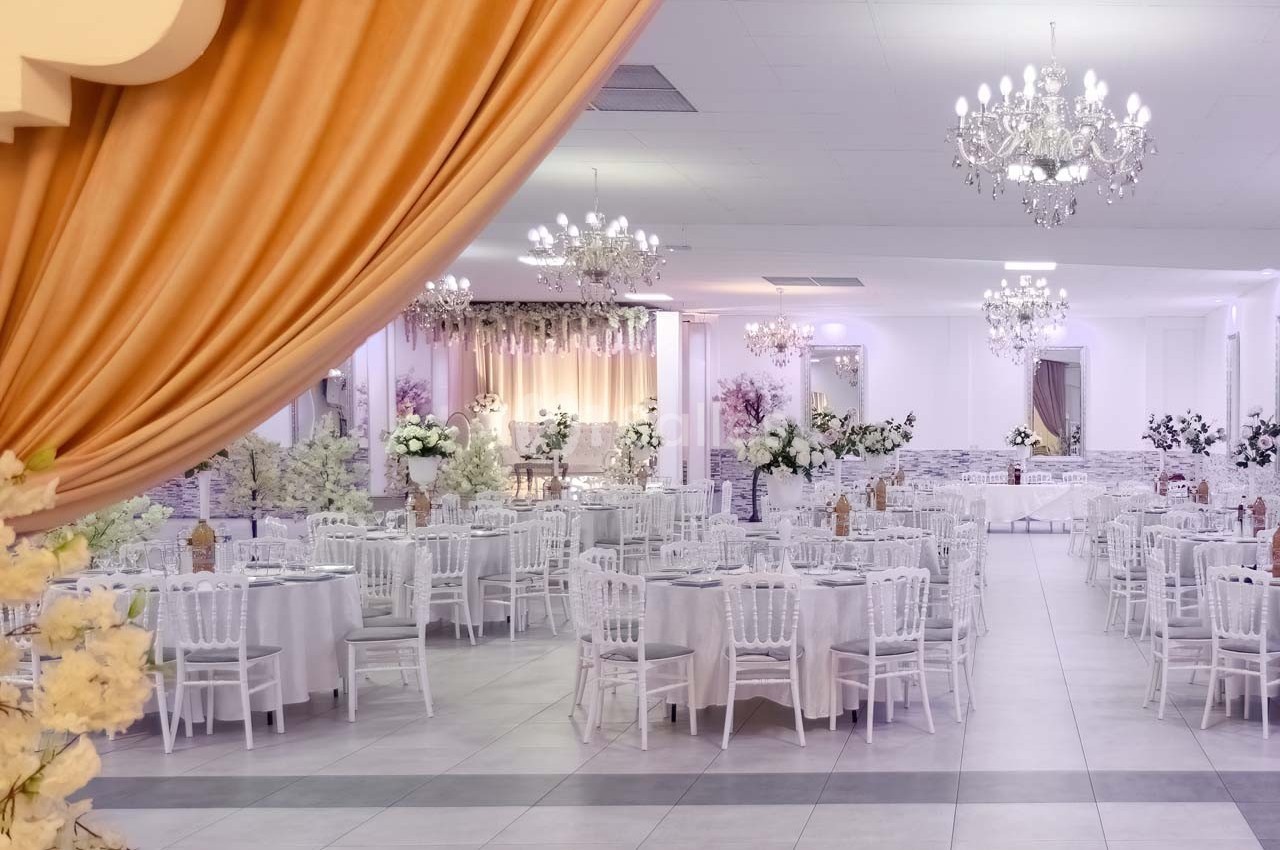 Salle de réception élégante avec tables rondes dressées, décorations florales et lustres suspendus.