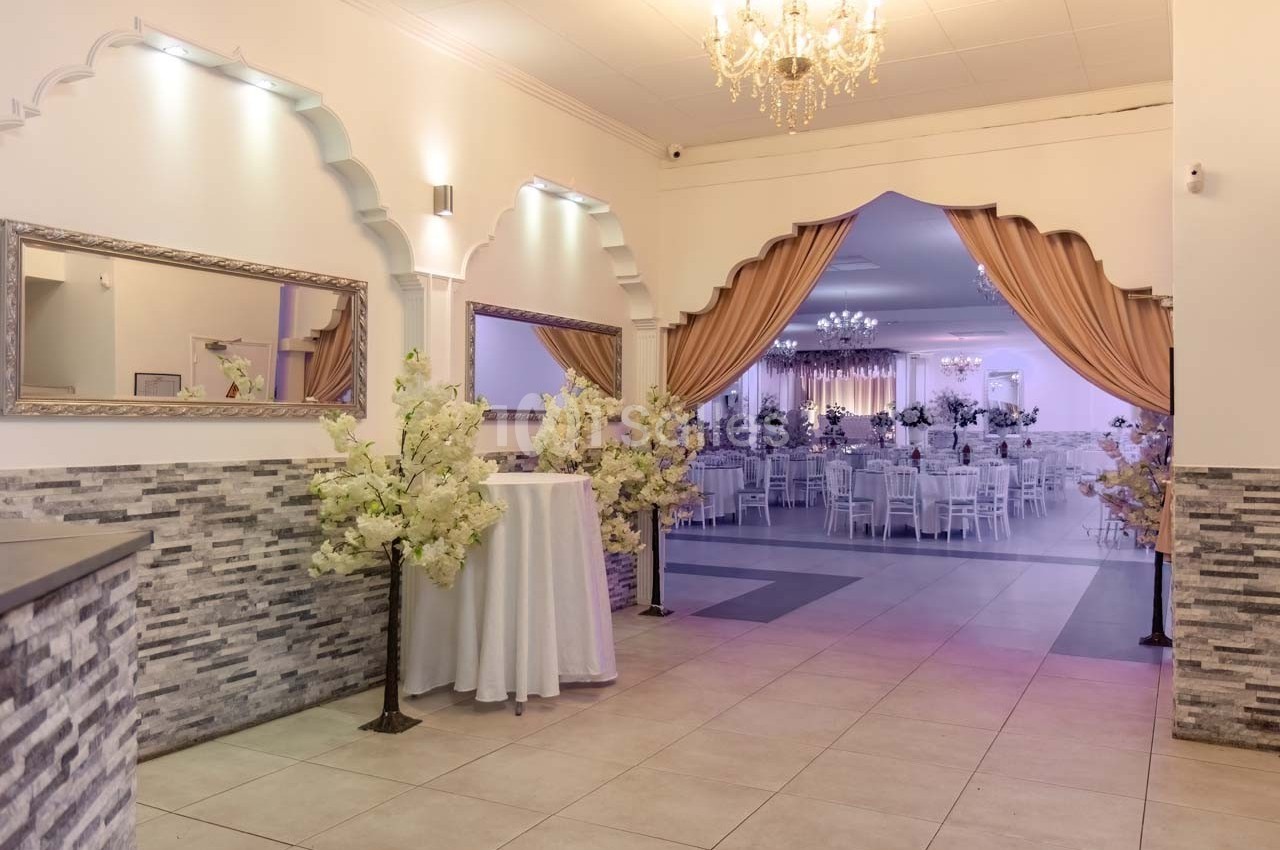 Salle de réception élégante avec rideaux dorés, lustres et tables décorées visibles en arrière-plan.