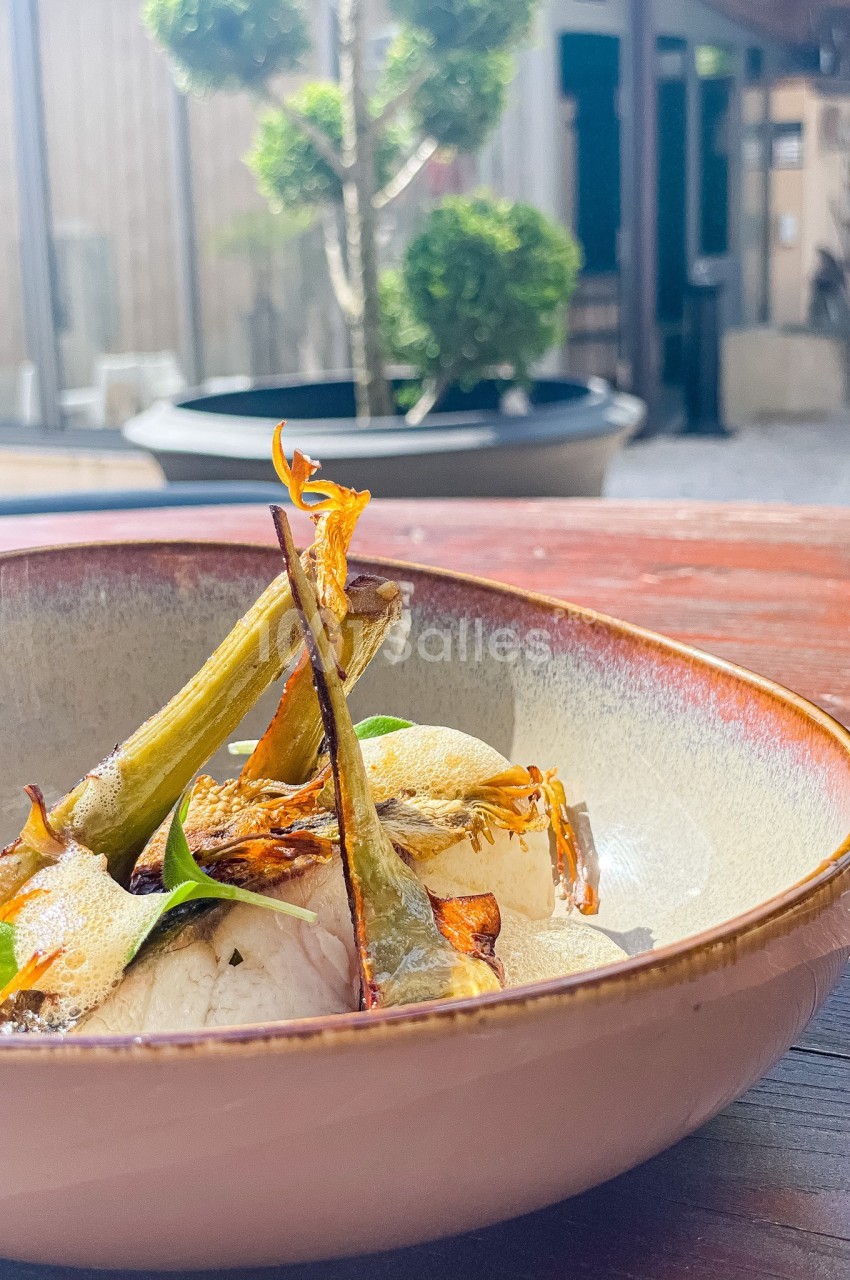 Assiette en céramique contenant un plat garni de légumes grillés, posée sur une table en bois en extérieur.