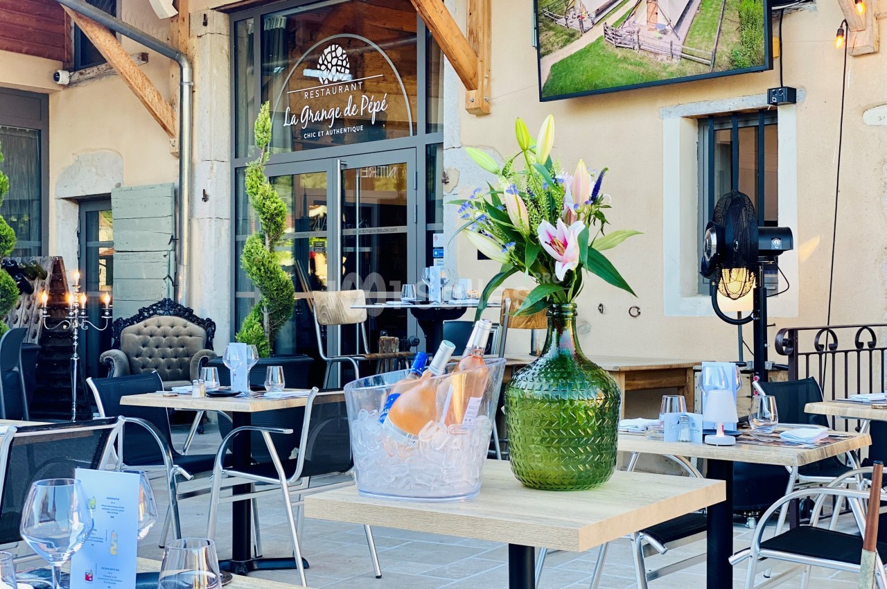 Terrasse d’un restaurant avec tables dressées, vase de fleurs et seau à glace contenant des bouteilles de vin.