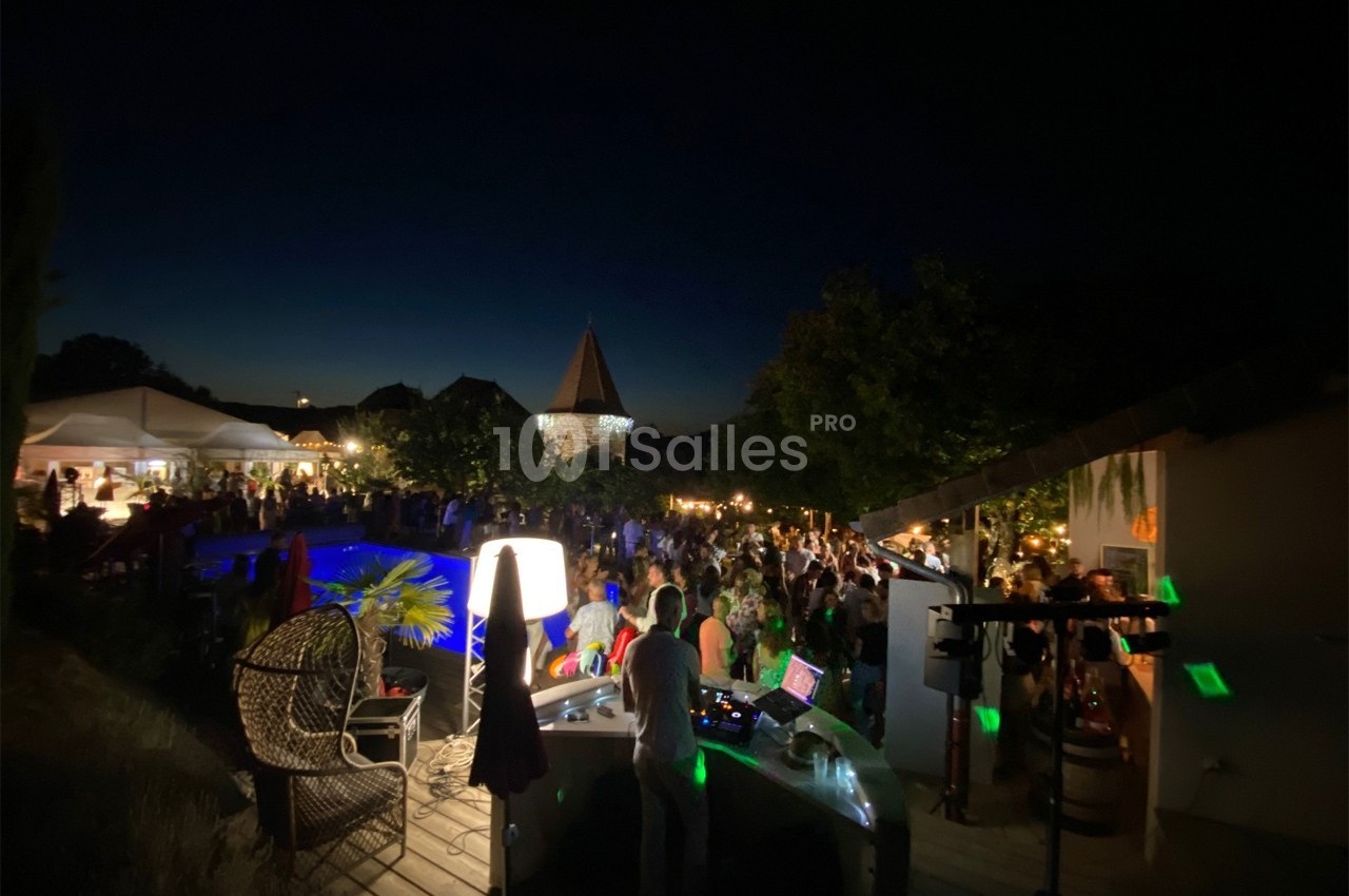 Fête nocturne en extérieur avec DJ, piscine éclairée et invités rassemblés sous des lumières tamisées.