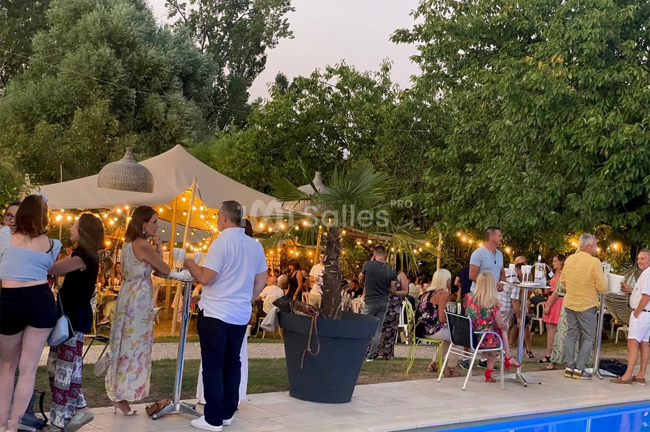 Personnes rassemblées près d'une piscine dans un jardin éclairé par des guirlandes lumineuses, ambiance festive en soirée.