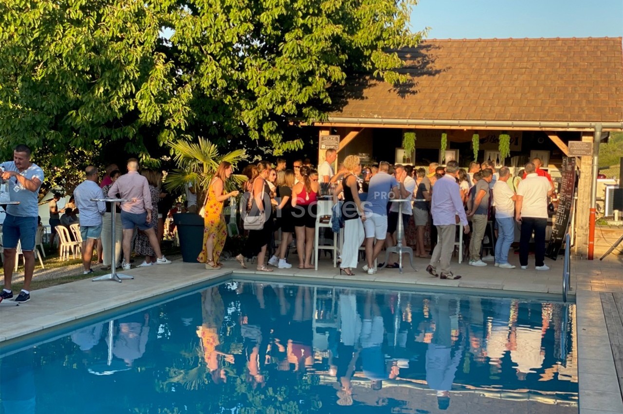 Groupe de personnes rassemblées près d'une piscine, devant un bar extérieur, sous un ciel dégagé en fin de journée.