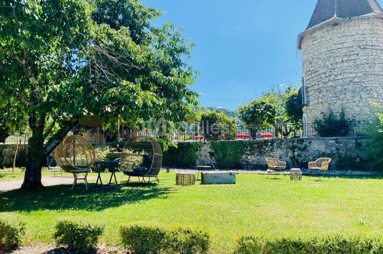 Jardin verdoyant avec chaises en rotin, arbres ombragés et une tour en pierre en arrière-plan.