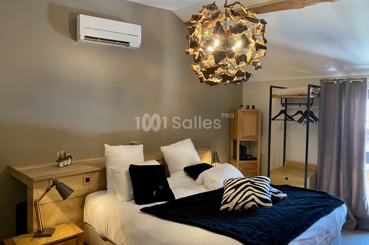 Chambre avec lit double, linge de lit sombre, luminaire en bois, climatisation murale et mobilier en bois clair.