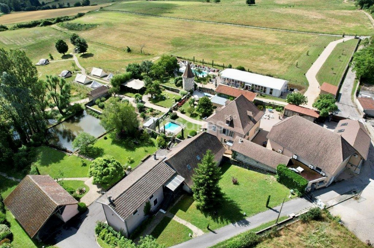 Vue aérienne d'un domaine rural avec plusieurs bâtiments, un étang, une piscine et des espaces verts environnants.