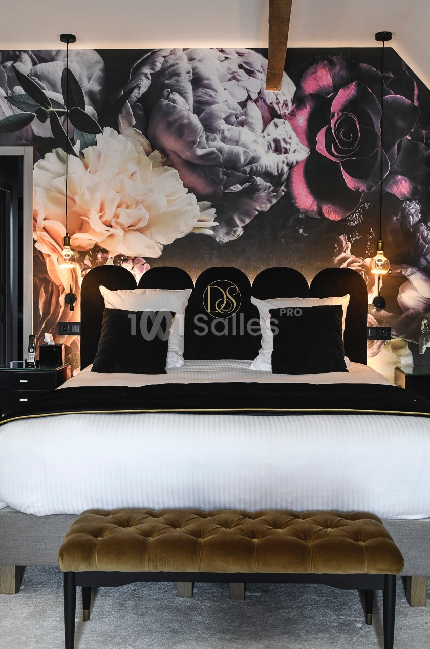 Lit double avec tête de lit noire, coussins noirs et mur décoré d'une fresque florale sombre dans une chambre élégante.