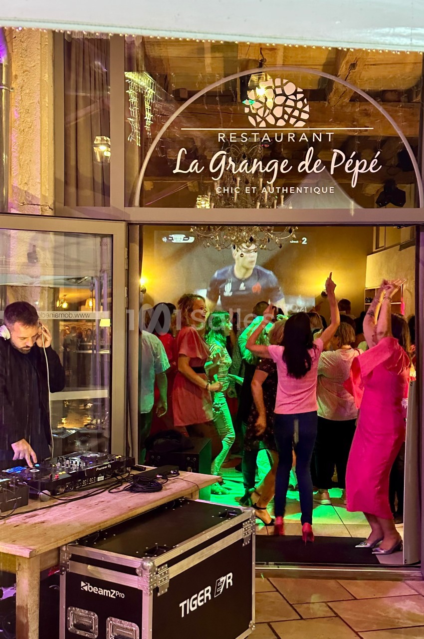 Des personnes dansent à l'intérieur d'un restaurant, avec un DJ jouant de la musique à l'extérieur près de l'entrée.