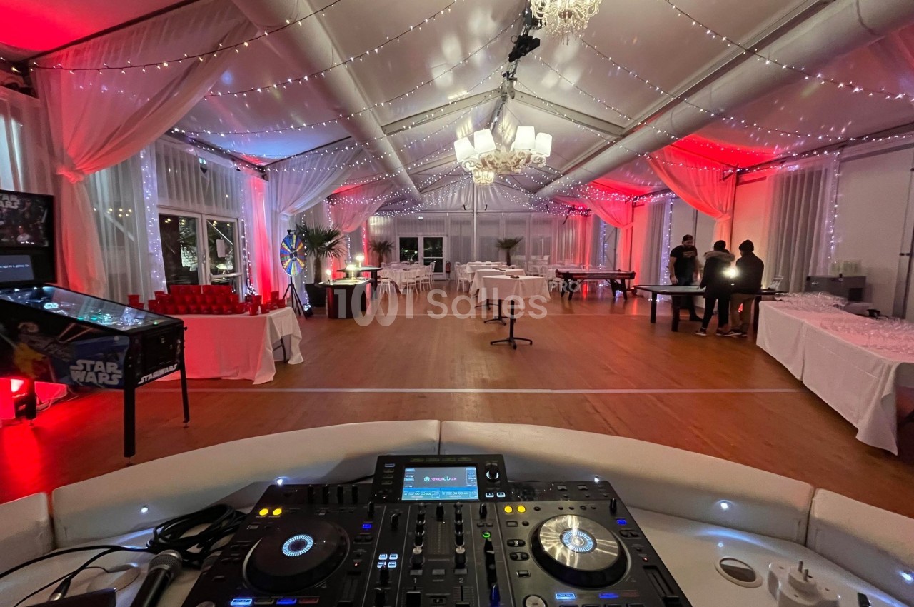 Salle de réception décorée avec des guirlandes lumineuses, vue depuis une table de mixage au premier plan.