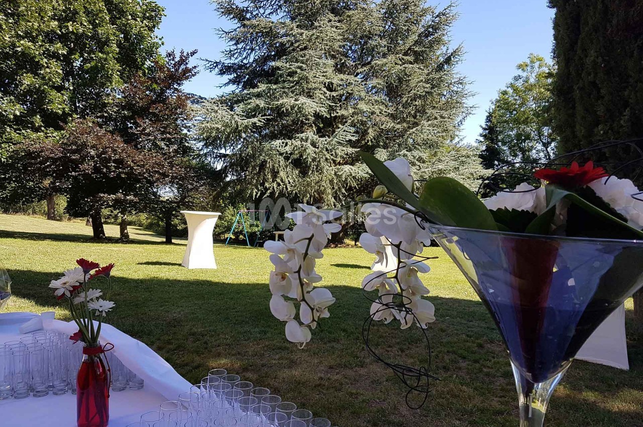 Table dressée en extérieur avec des fleurs blanches et rouges, vue sur un jardin arboré par une journée ensoleillée.
