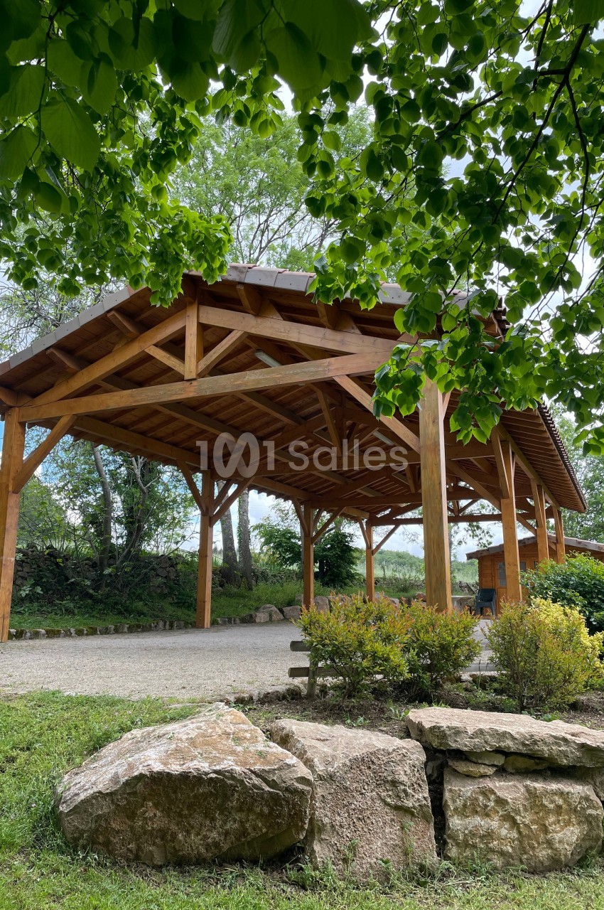 Abri en bois avec toit en tuiles, entouré de végétation et de pierres dans un cadre naturel.