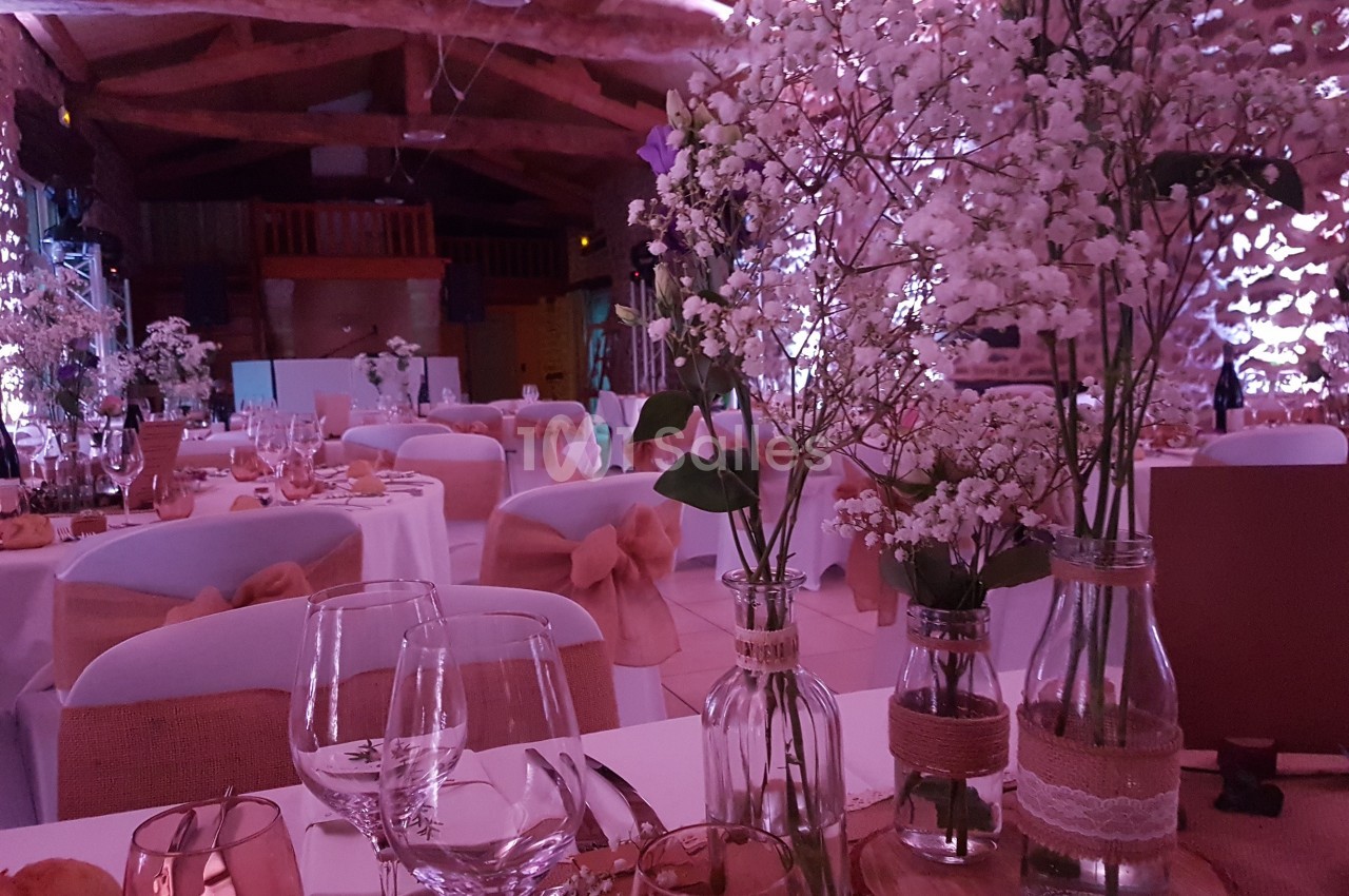 Salle de réception décorée avec des fleurs blanches, des tables dressées et une ambiance lumineuse tamisée.