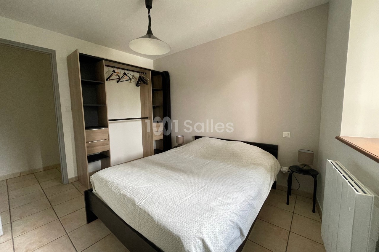 Chambre lumineuse avec lit double, armoire ouverte, table de chevet et sol en carrelage beige.