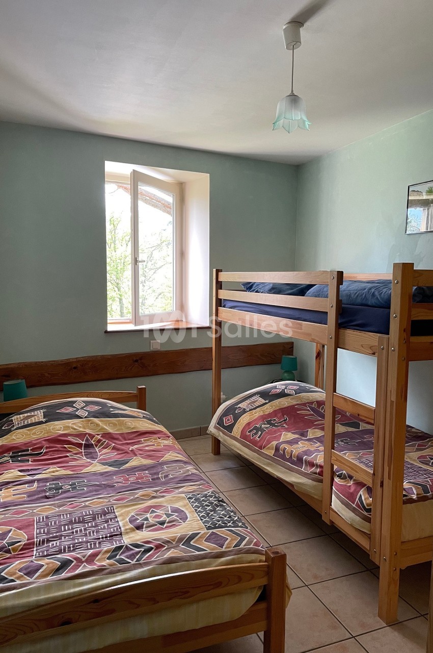 Chambre avec deux lits simples et un lit superposé en bois, éclairée par une fenêtre donnant sur l'extérieur.