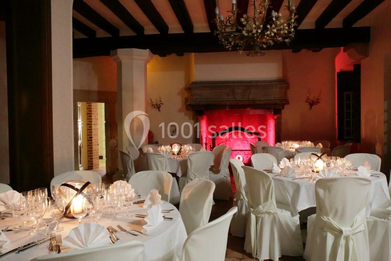 Salle de réception élégante avec tables rondes dressées, nappes blanches et éclairage chaleureux.