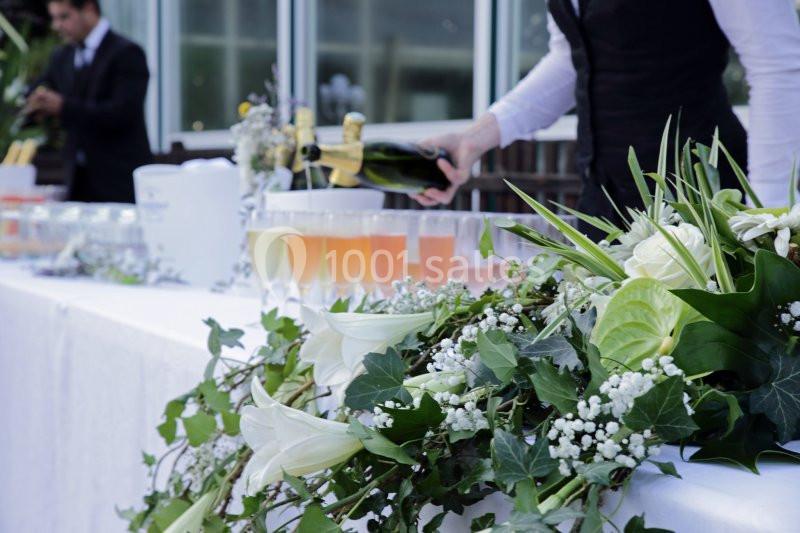 Un serveur verse du champagne sur une table décorée de fleurs blanches et de verdure lors d'un événement.