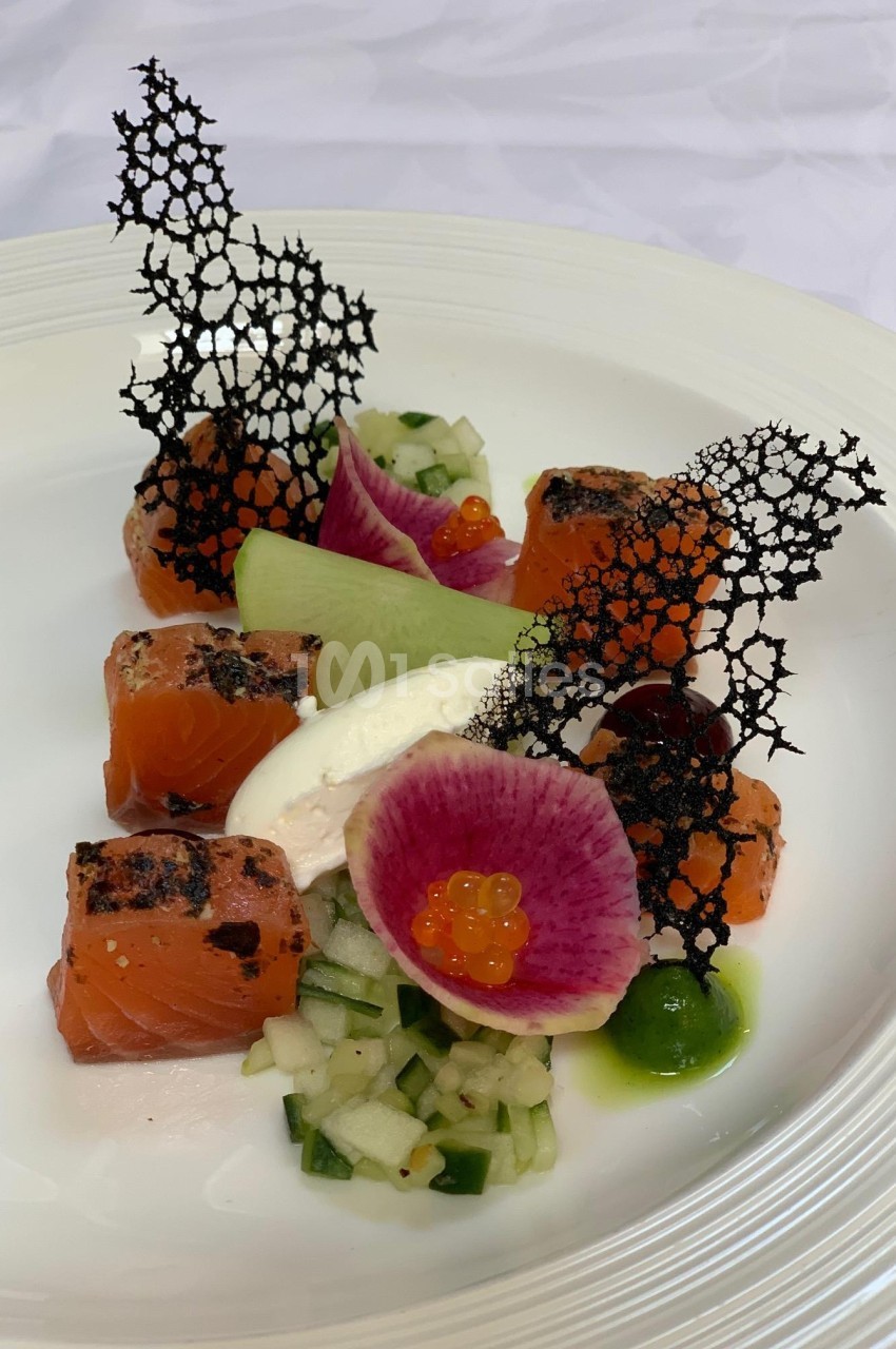 Assiette gastronomique avec saumon mariné, légumes croquants, crème, radis coloré, perles d'orange et décor noir ajouré.
