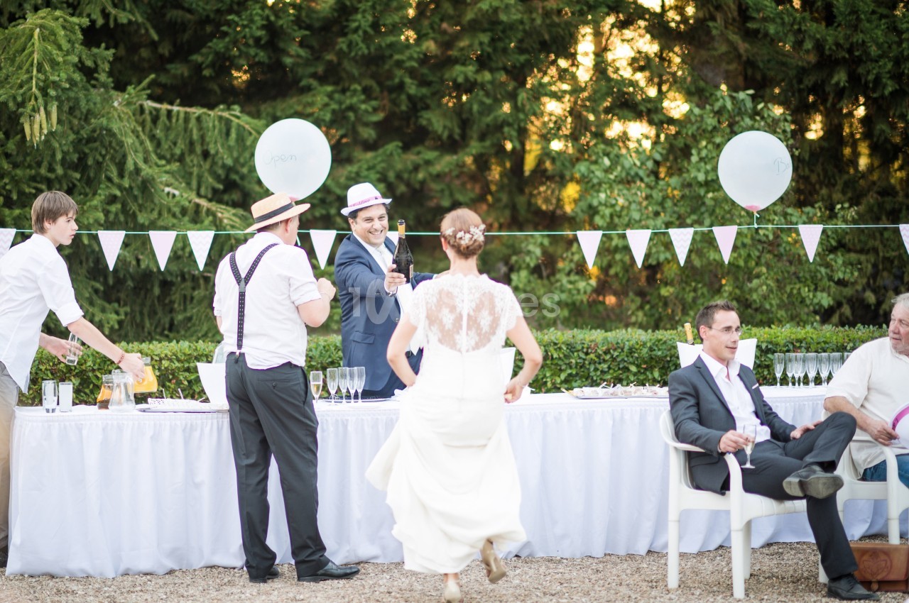 Un mariage en extérieur avec des invités discutant près d'une table décorée, une mariée de dos s'approche.