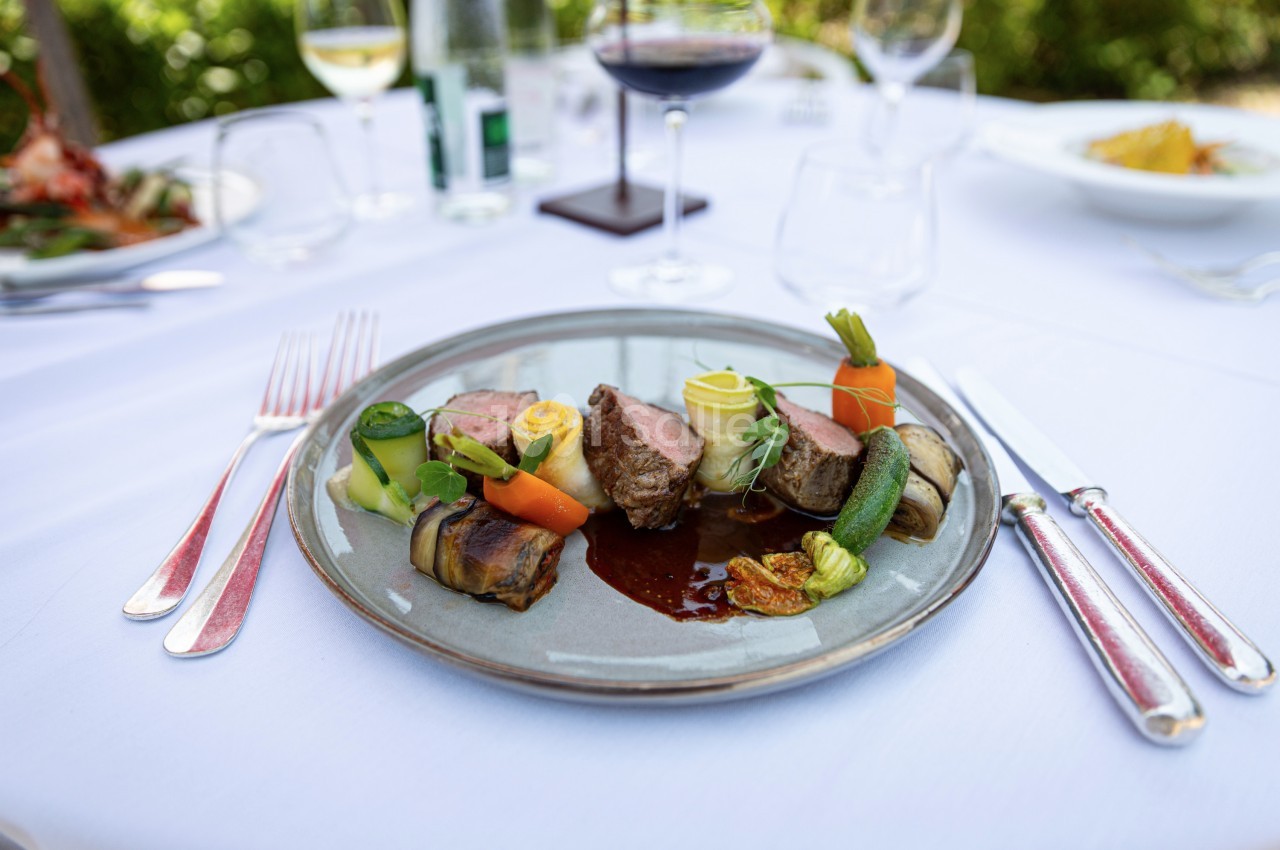 Assiette gastronomique avec viande, légumes variés et sauce, servie sur une table dressée en extérieur.