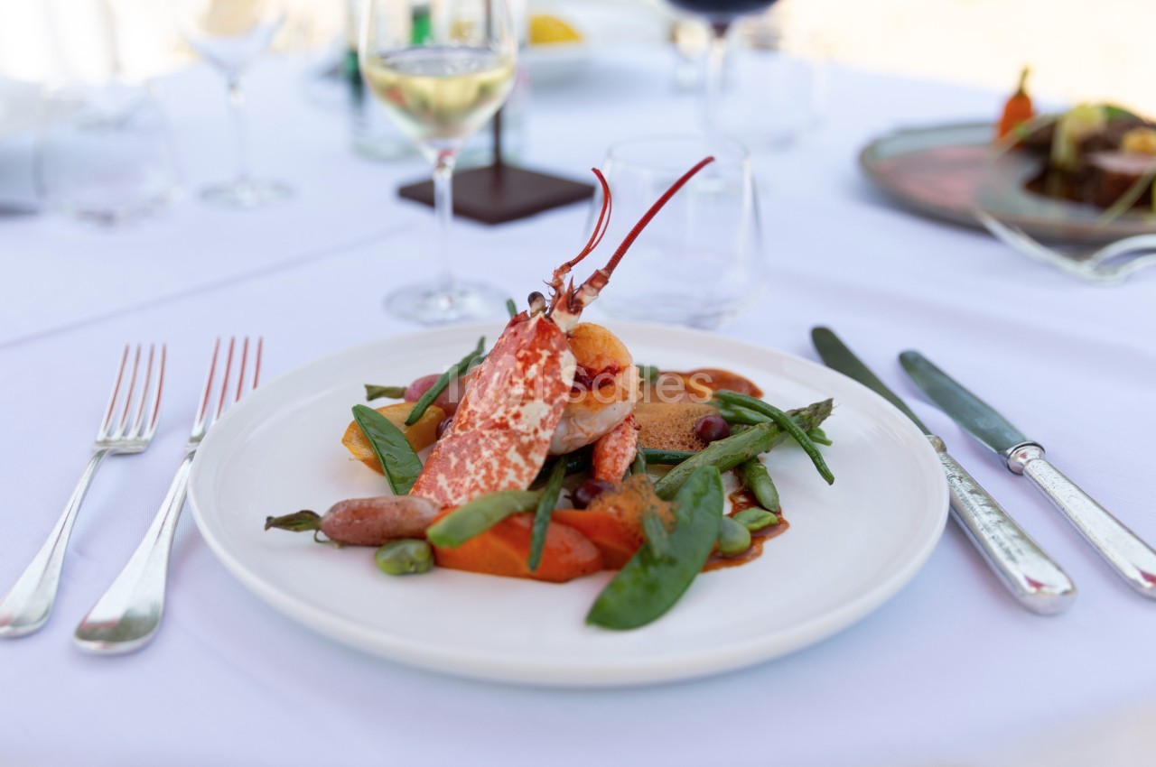 Assiette de homard accompagné de légumes variés, servie sur une table dressée avec couverts et verres à vin.