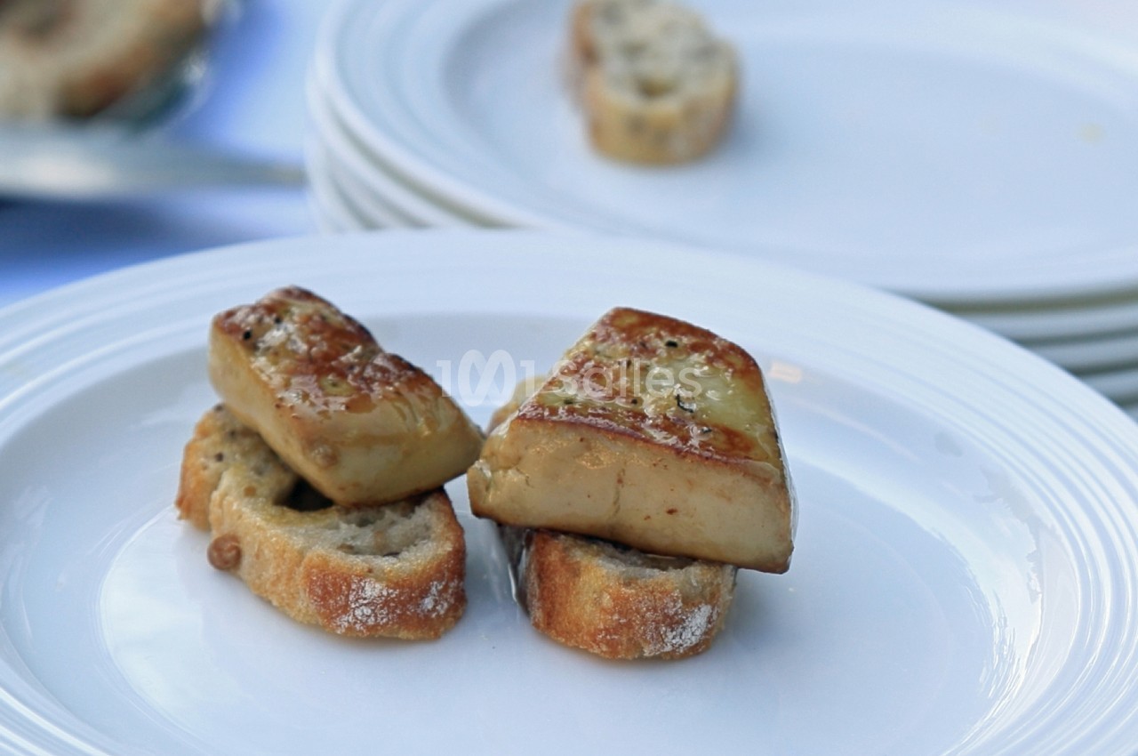 Tranches de foie gras posées sur des morceaux de pain grillé, servies sur une assiette blanche.