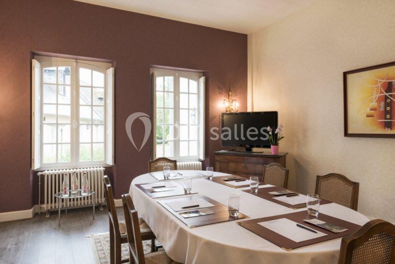 Salle de réunion lumineuse avec une grande table, des chaises en bois, des fenêtres ouvertes et une télévision sur un meuble.
