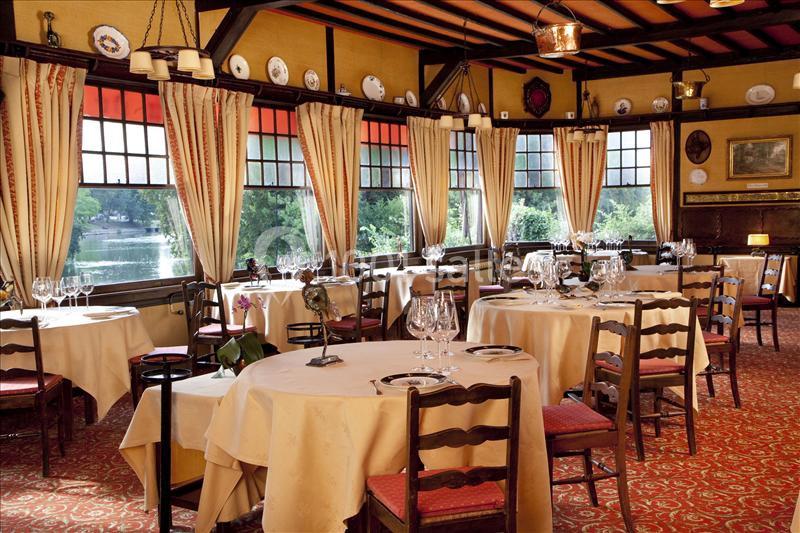 Salle de restaurant élégante avec nappes blanches, grandes fenêtres donnant sur un paysage verdoyant et décoration…