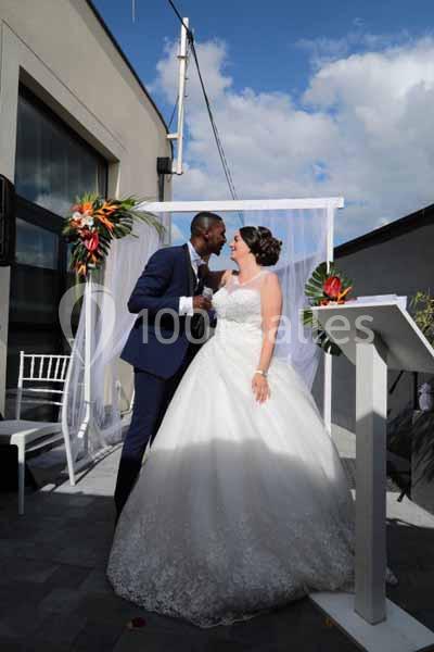 Un couple en tenue de mariage se tient devant une arche décorée de fleurs lors d'une cérémonie en extérieur.