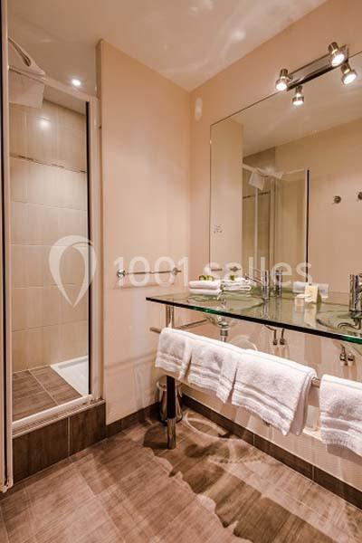 Salle de bain avec douche, miroir éclairé, lavabo en verre, serviettes blanches et carrelage beige au sol.