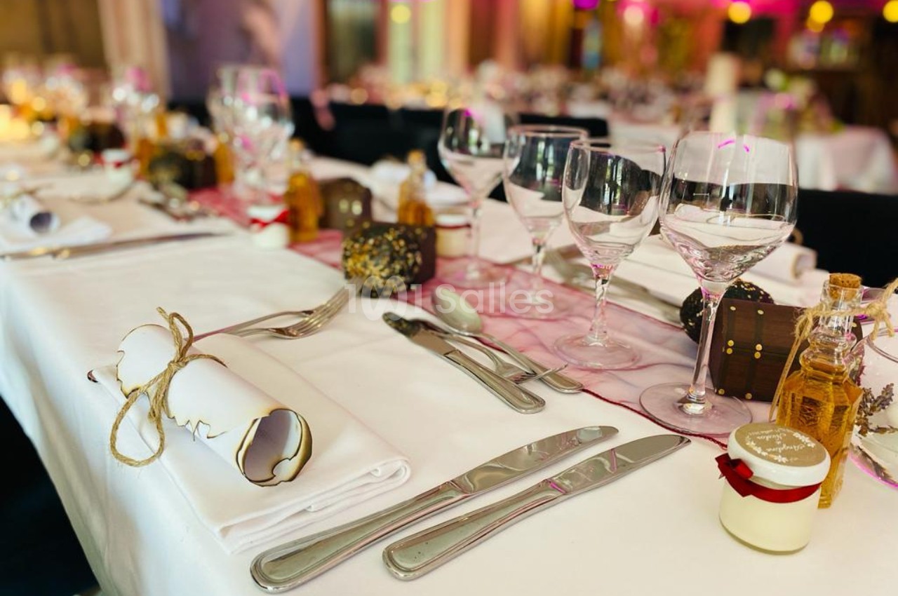 Table dressée pour un repas festif avec nappes blanches, couverts, verres, crackers et petits cadeaux décoratifs.