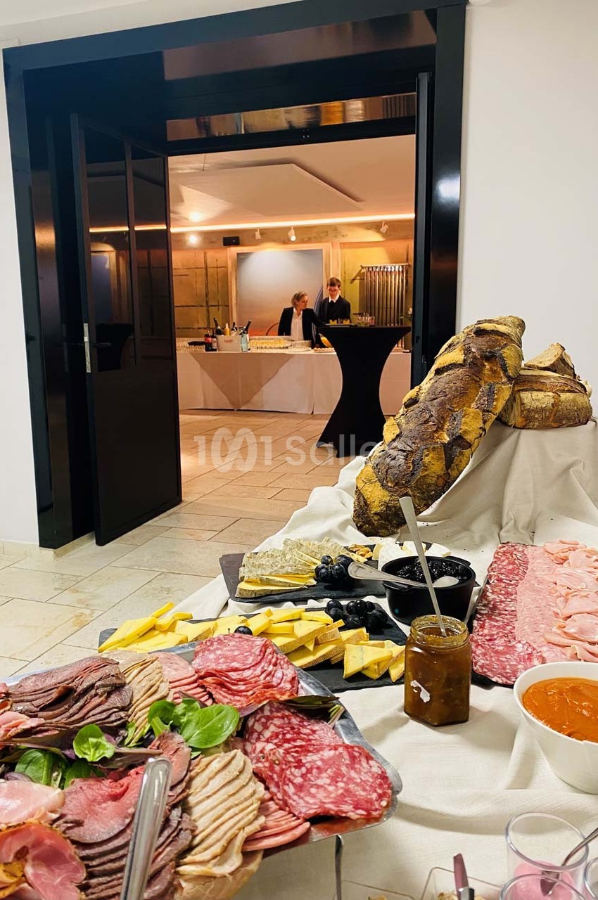 Plateau de charcuterie, fromages, pain et condiments disposés sur une table lors d'un événement en intérieur.