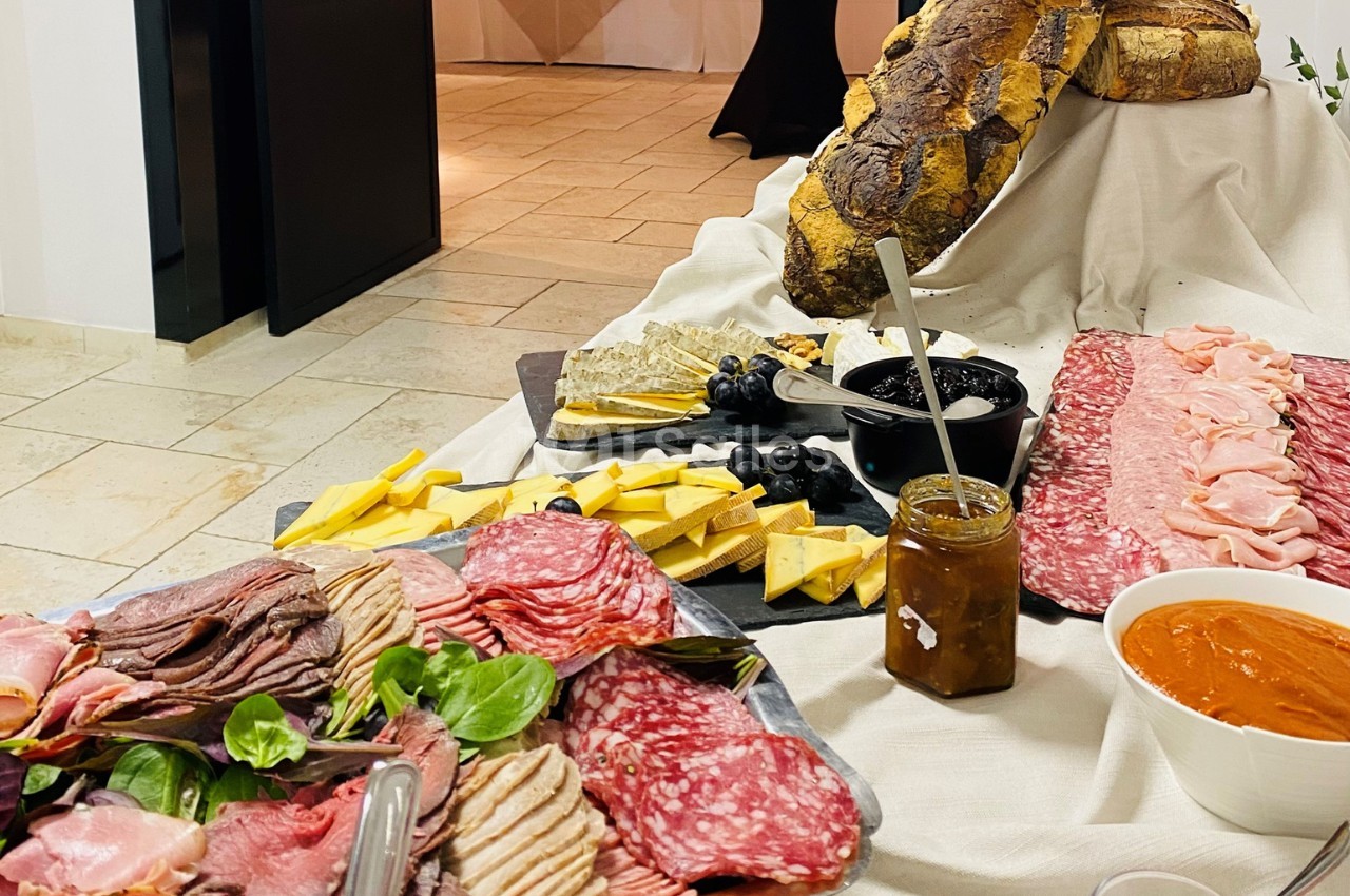 Plateau de charcuterie, fromages, pain, olives et confitures disposés sur une table pour un buffet.