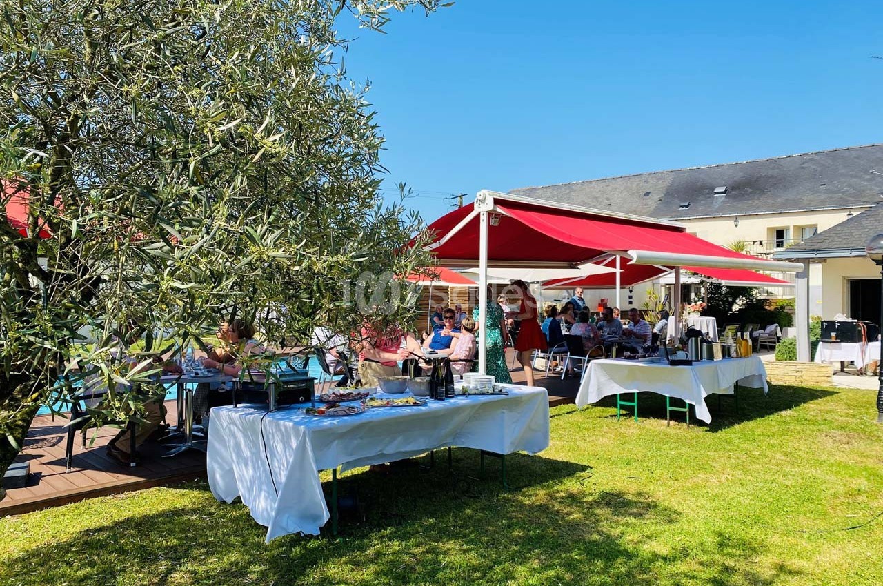 Des tables dressées sous des parasols rouges dans un jardin, avec des convives profitant d'un repas en plein air.