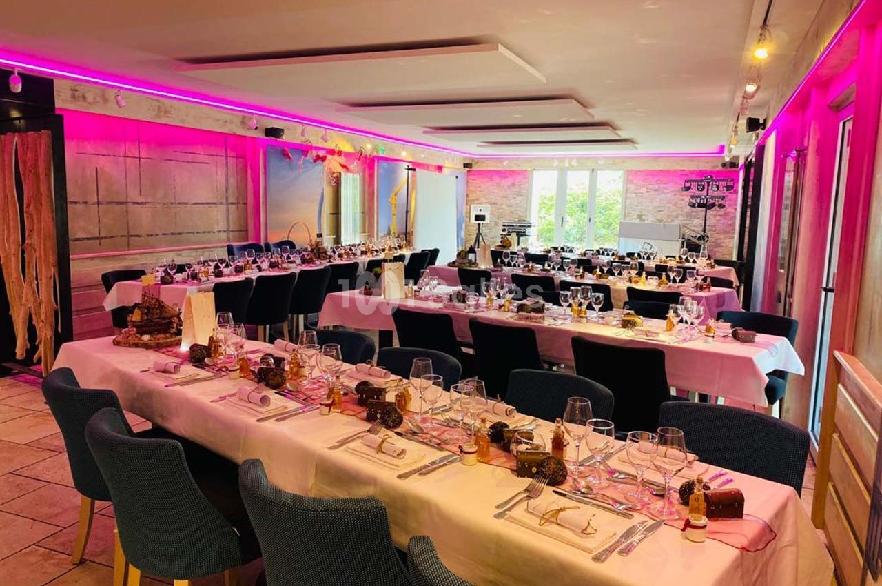Salle décorée pour un repas festif, avec tables dressées, nappes blanches, chaises bleues et éclairage rose.