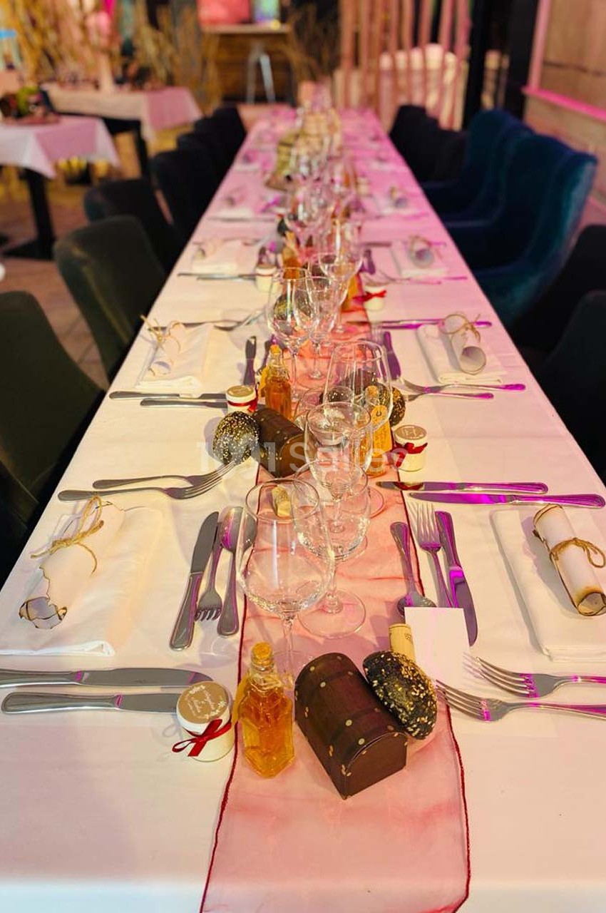 Table dressée pour un repas festif avec nappes blanches, verres, couverts, décorations et petits coffrets cadeaux.