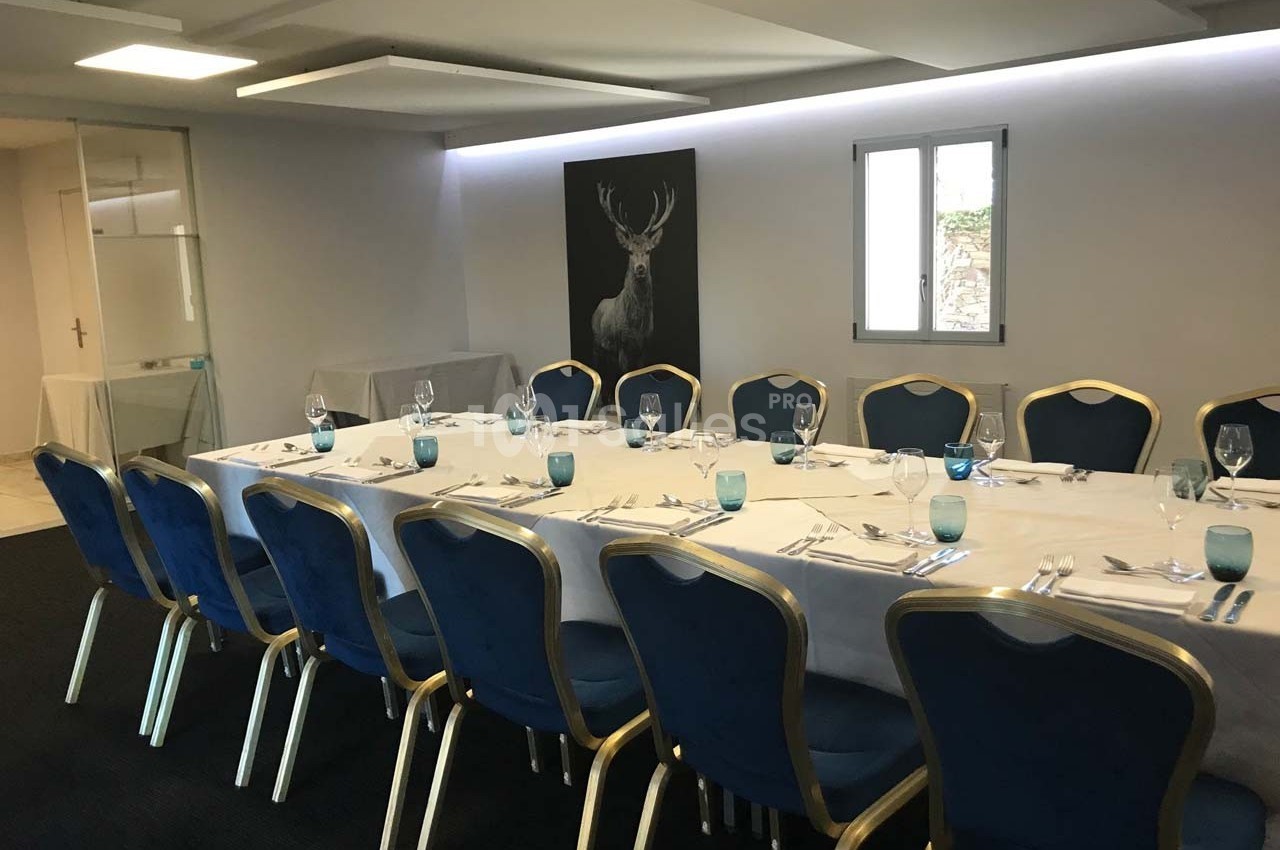 Salle de réunion avec une grande table rectangulaire dressée, entourée de chaises bleues et éclairée par une fenêtre.