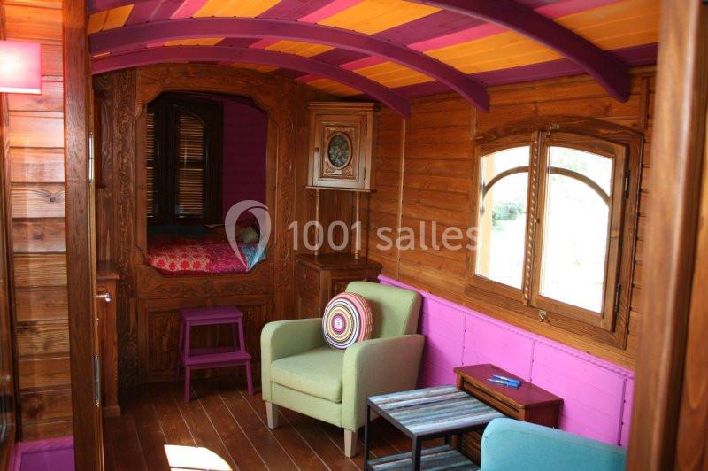 Intérieur d'une roulotte en bois avec un coin salon coloré, un lit encastré et des détails décoratifs.