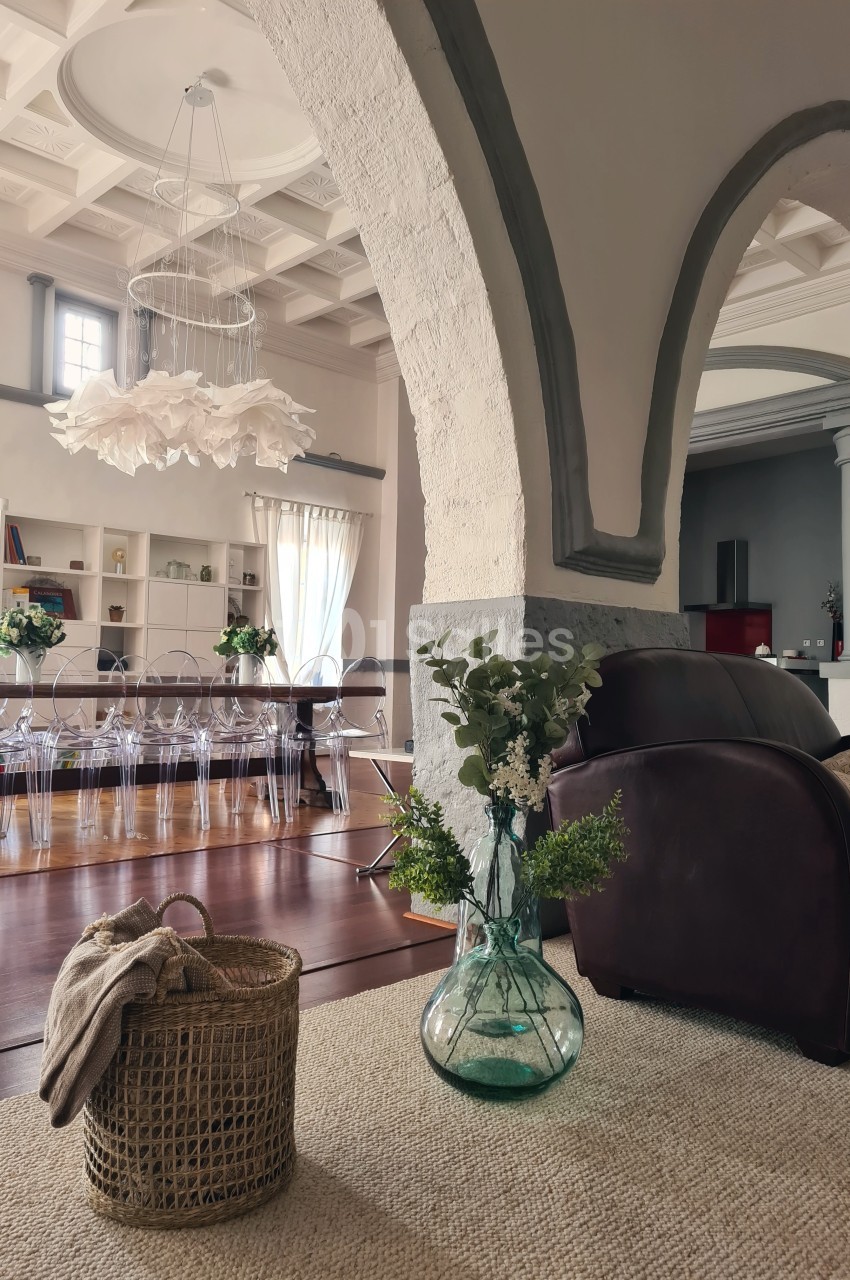 Intérieur lumineux avec salon, fauteuil en cuir, panier en osier, vase fleuri et salle à manger en arrière-plan.