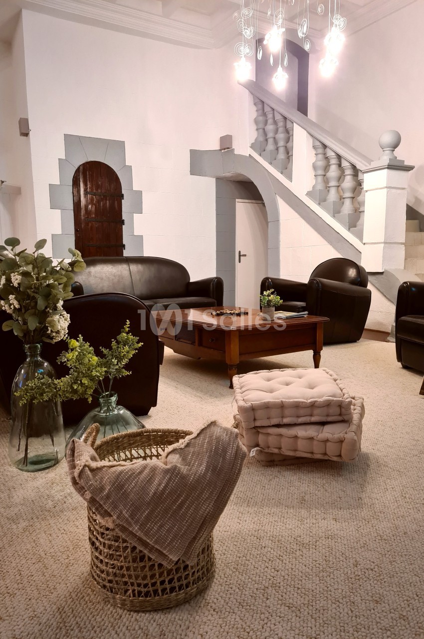 Salon lumineux avec fauteuils en cuir, table basse en bois, paniers en osier, escaliers et décorations florales.